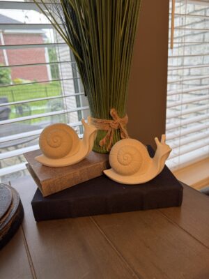 Two white ceramic snail figurines on books
